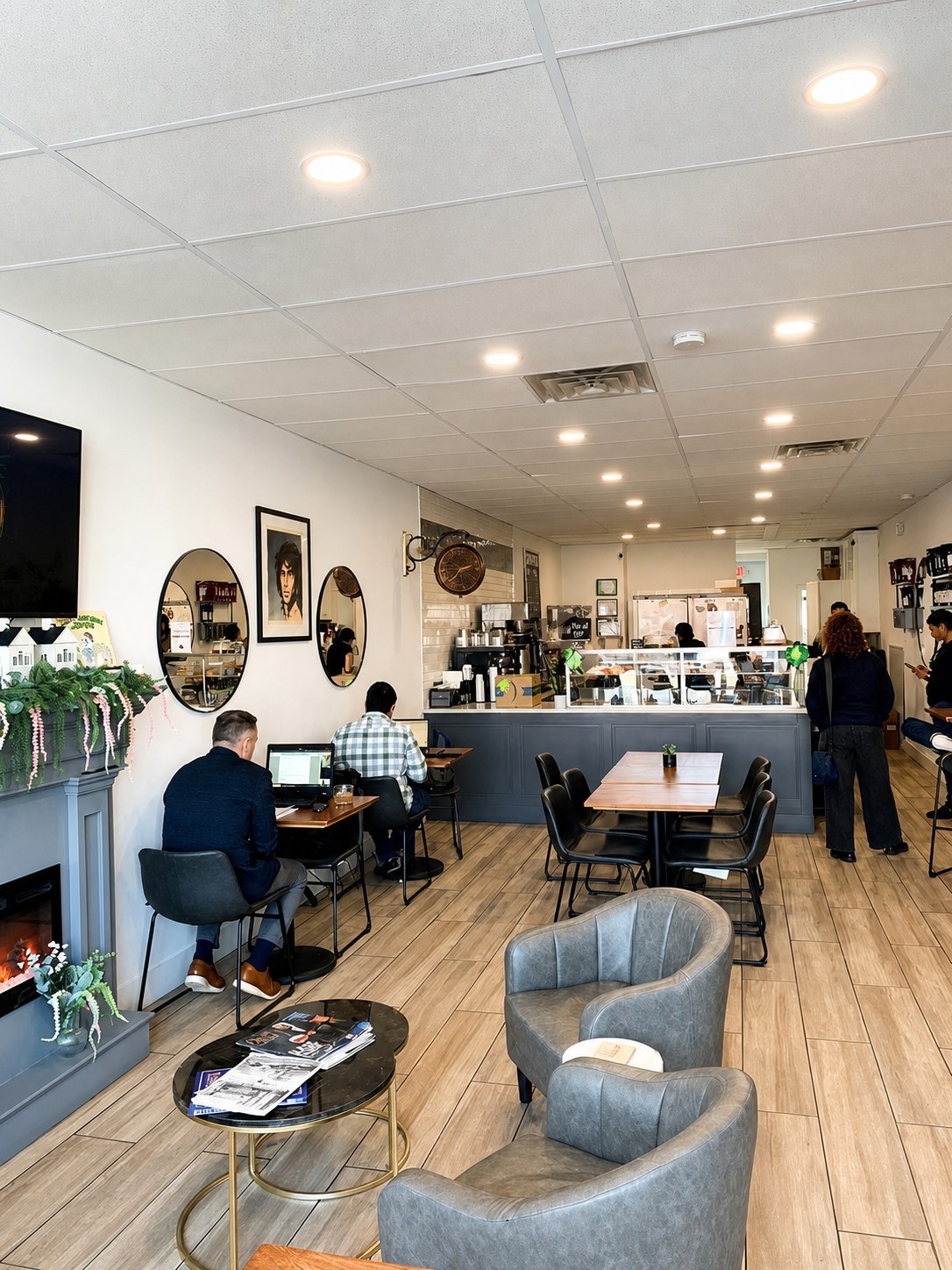 The café interior with a grey fireplace, armchairs, and guests working on laptops near the counter